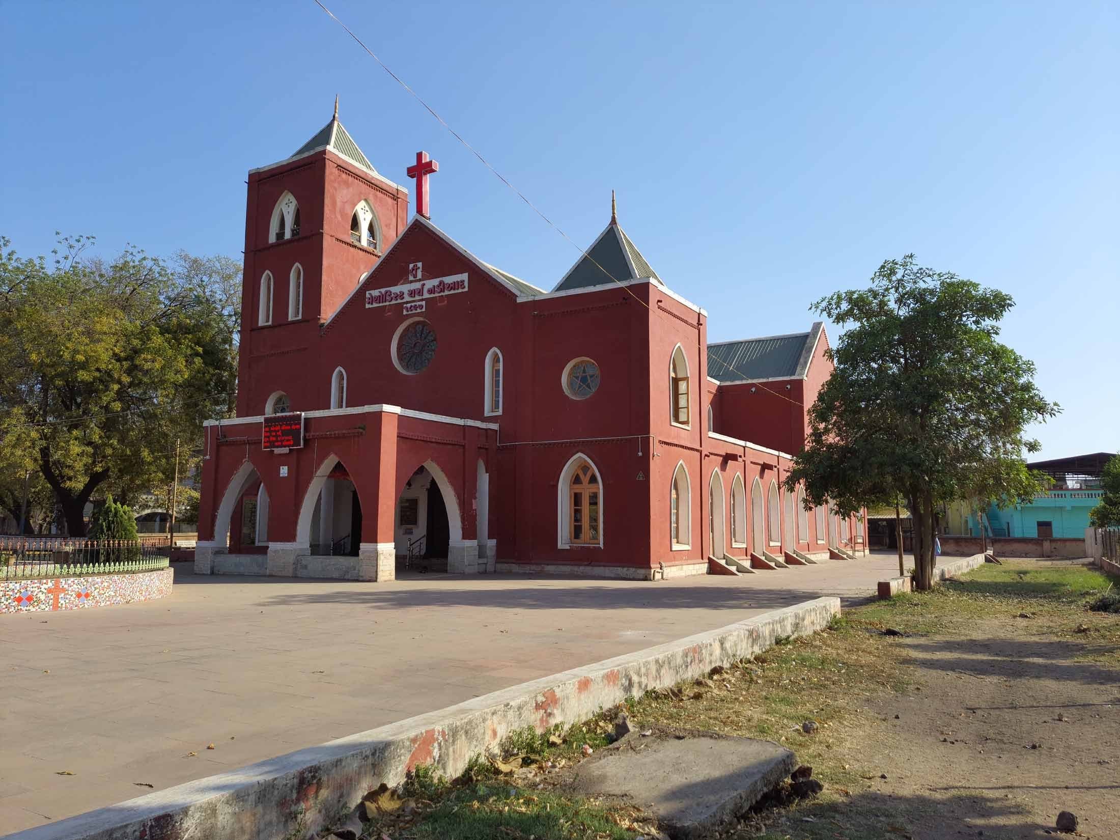 The west front of Methodist Church Nadiad, with its arched portico, rose window and star window, and the mosaic-tiled garden wall in the foreground.
