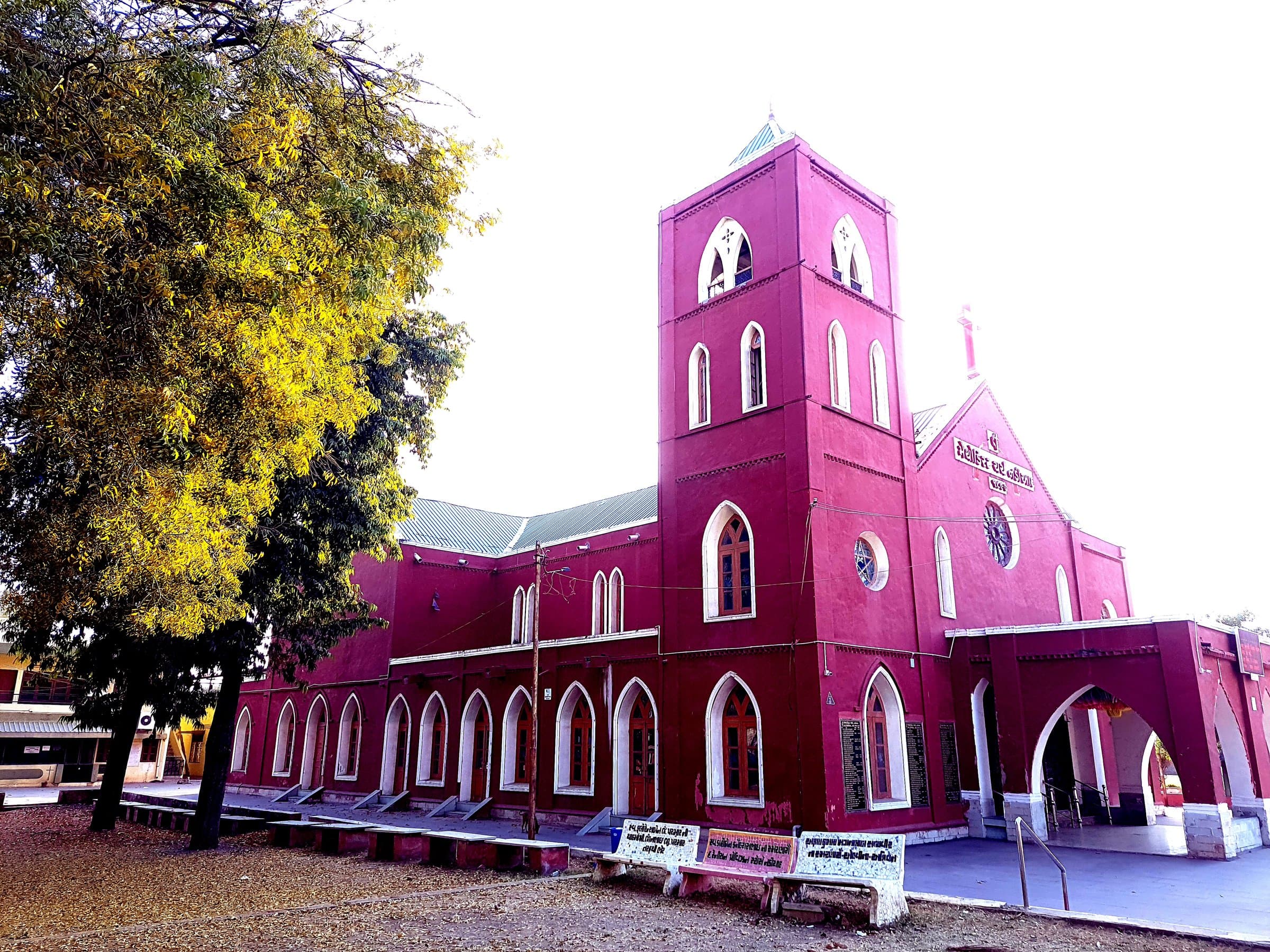 The side of Methodist Church Nadiad in the afternoon, its long arcade of pointed-arch windows framed by a flowering tree.
