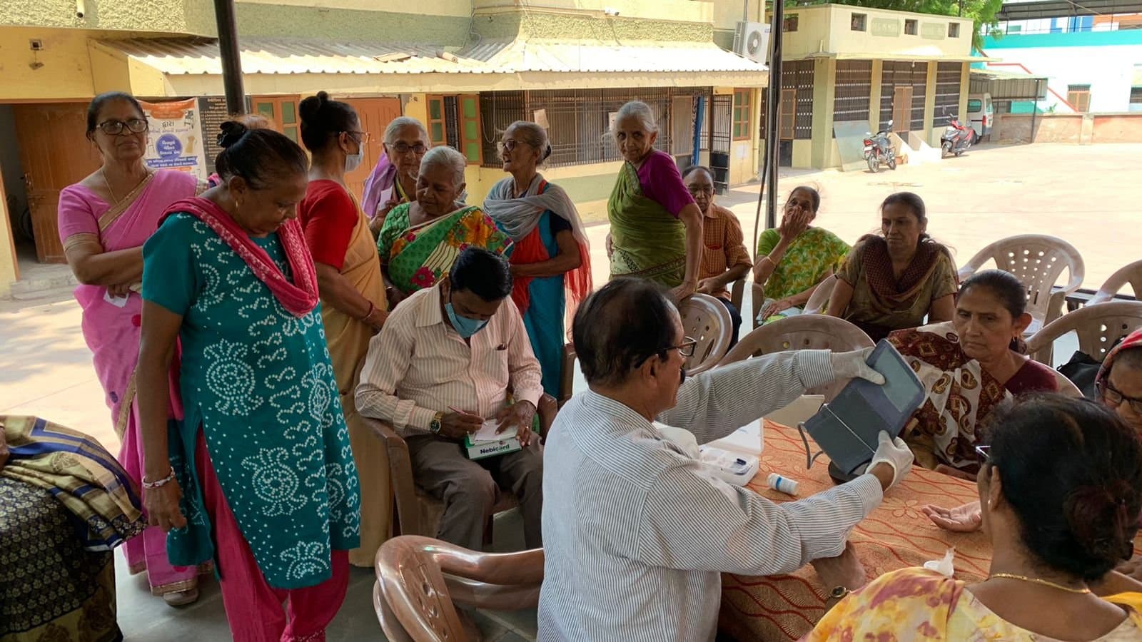 A medical volunteer checking blood pressure at the church health camp, with women of the congregation waiting nearby.