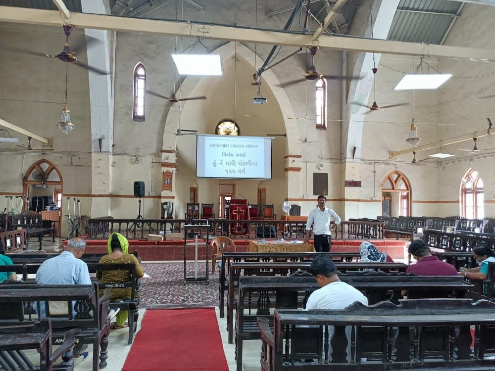 Inside the sanctuary of Methodist Church Nadiad during the 125th anniversary essay competition, with the pulpit, pews and chandeliers.