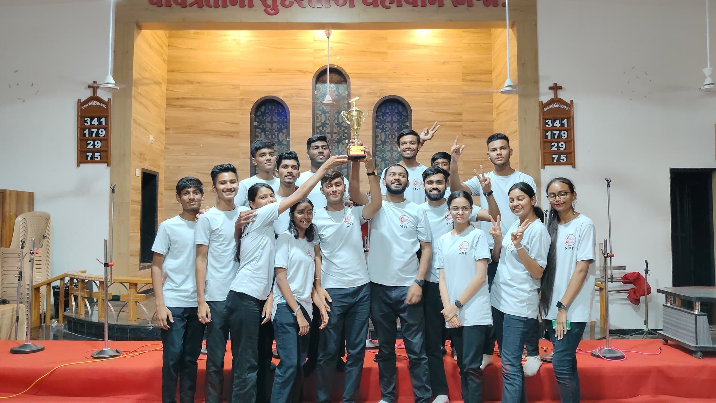 The Methodist Youth Fellowship holding up a trophy on the chancel steps, in matching MYF shirts.