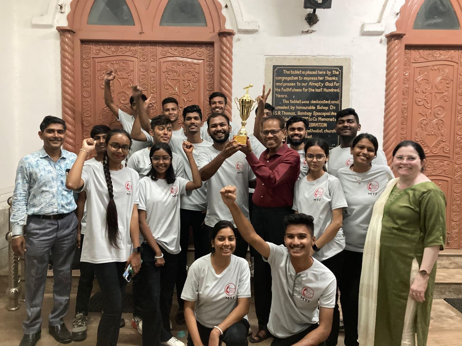 The Methodist Youth Fellowship celebrating with their trophy beside the centenary tablet in the church porch.